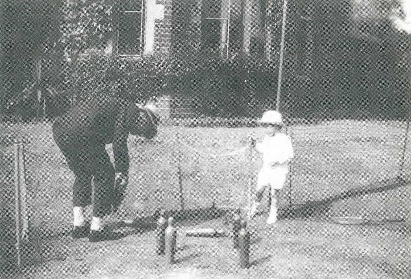 Photo of Alvan Birkett playing skittles with his son John. Alvan is bending down to pick up some skittles