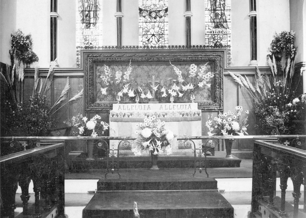 Photo of the altar, decorated with many flowers and the words ALLELUIA ALLELUIA prominently displayed, showing the oak panelling and reredos
