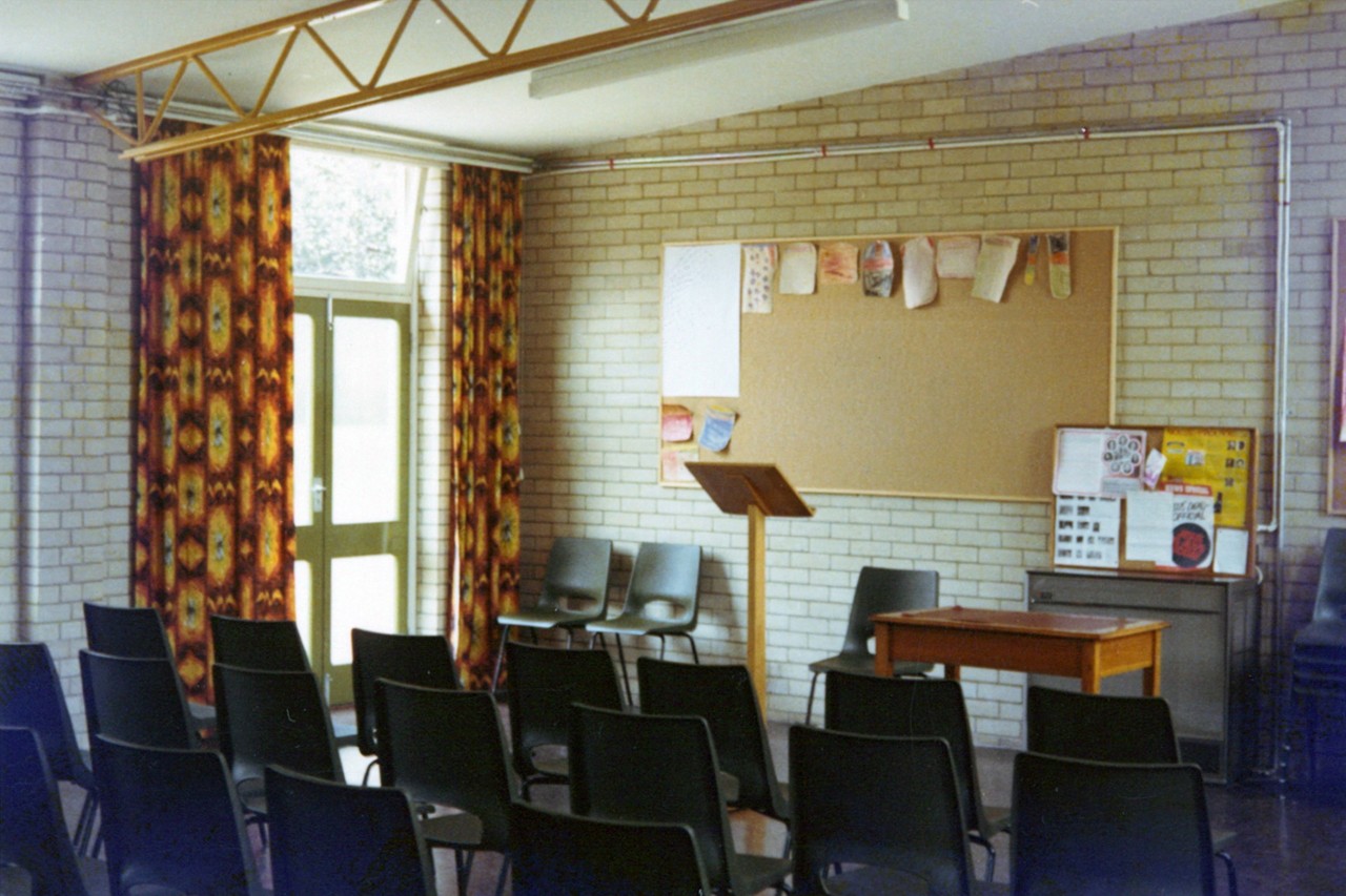 Photo showing the interior of the Vestry Hall with a simple lecturn, noticeboard and rows of chairs visible