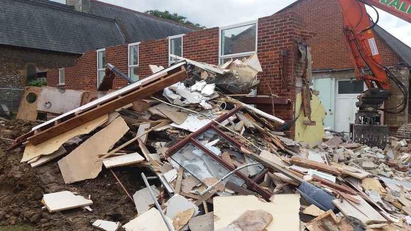 Photo showing the demolition of the Vestry Hall and Holly Room in progress, a pile of rubble in the foreground as the back wall remains